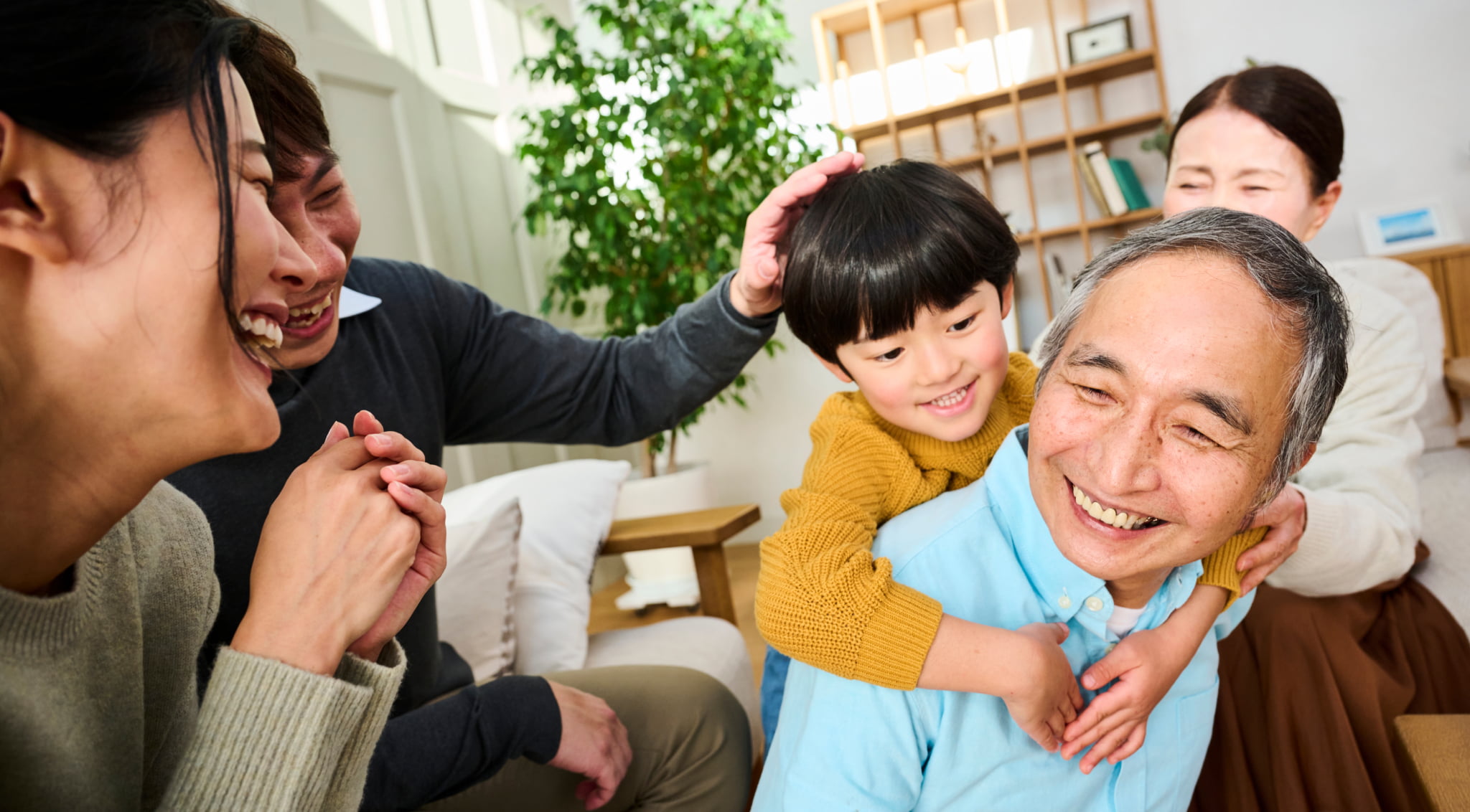 祖父に子どもが抱きつき、家族全員が笑顔で過ごしている家庭の風景